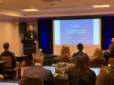 Ken Wisnefski at a podium presenting a slide titled Re-establishing Credibility and Integrity to Your Brand to a seated audience