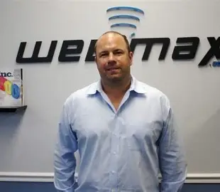 Ken Wisnefski standing in front of the WebiMax logo wall at the company office